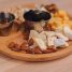 A close-up of a wooden tray featuring assorted cheeses, olives, nuts, and honey.